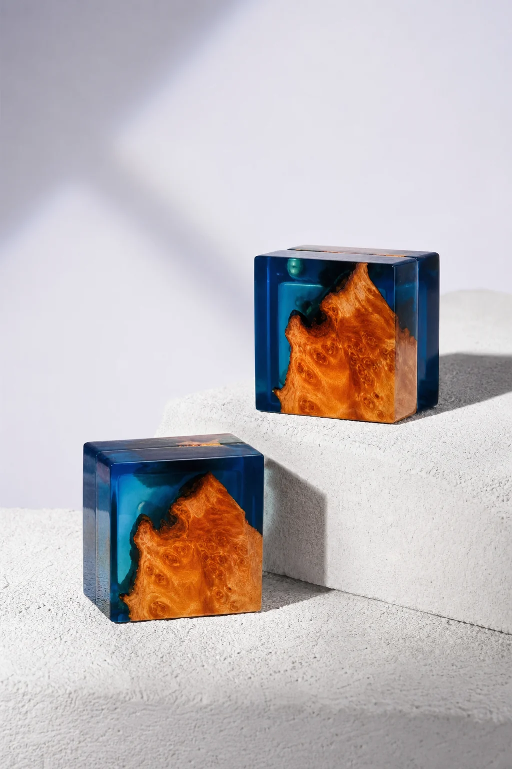 Two closed blue wood and resin GOGOJSM ring boxes arranged on white stone blocks